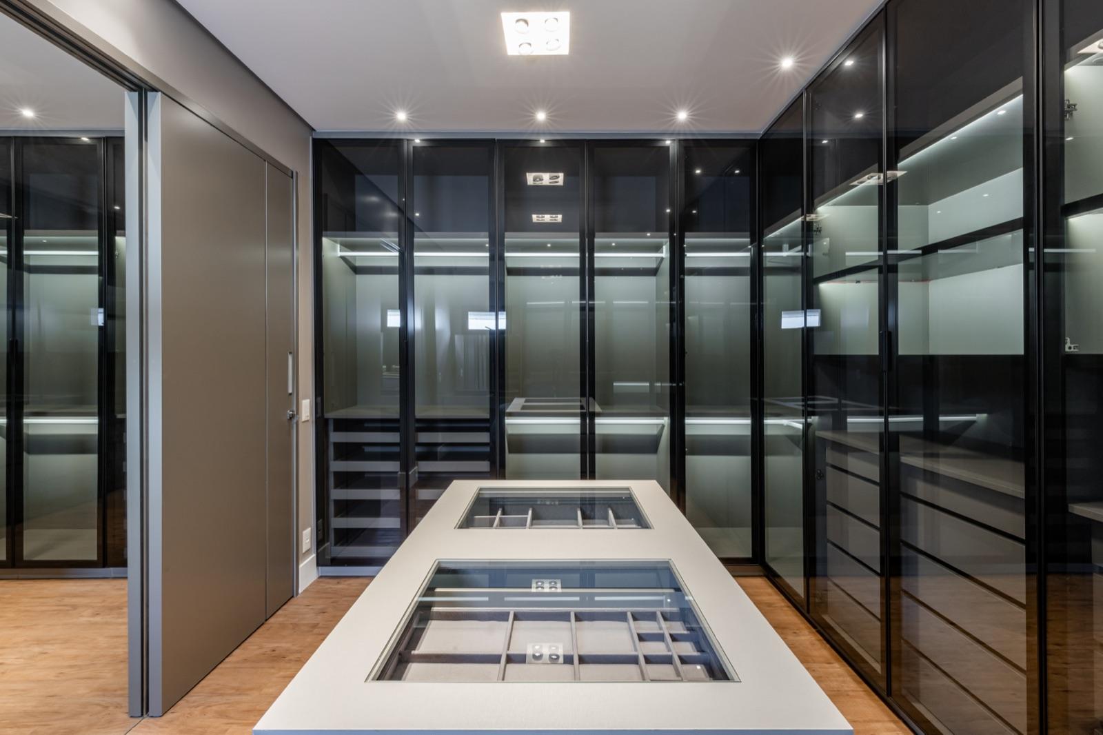 Closet com portas em vidro fumê e iluminação técnica.